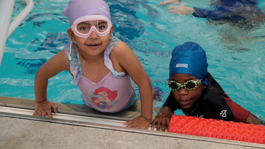 Two young swimmers in goggles and swim caps holding the pool wall
