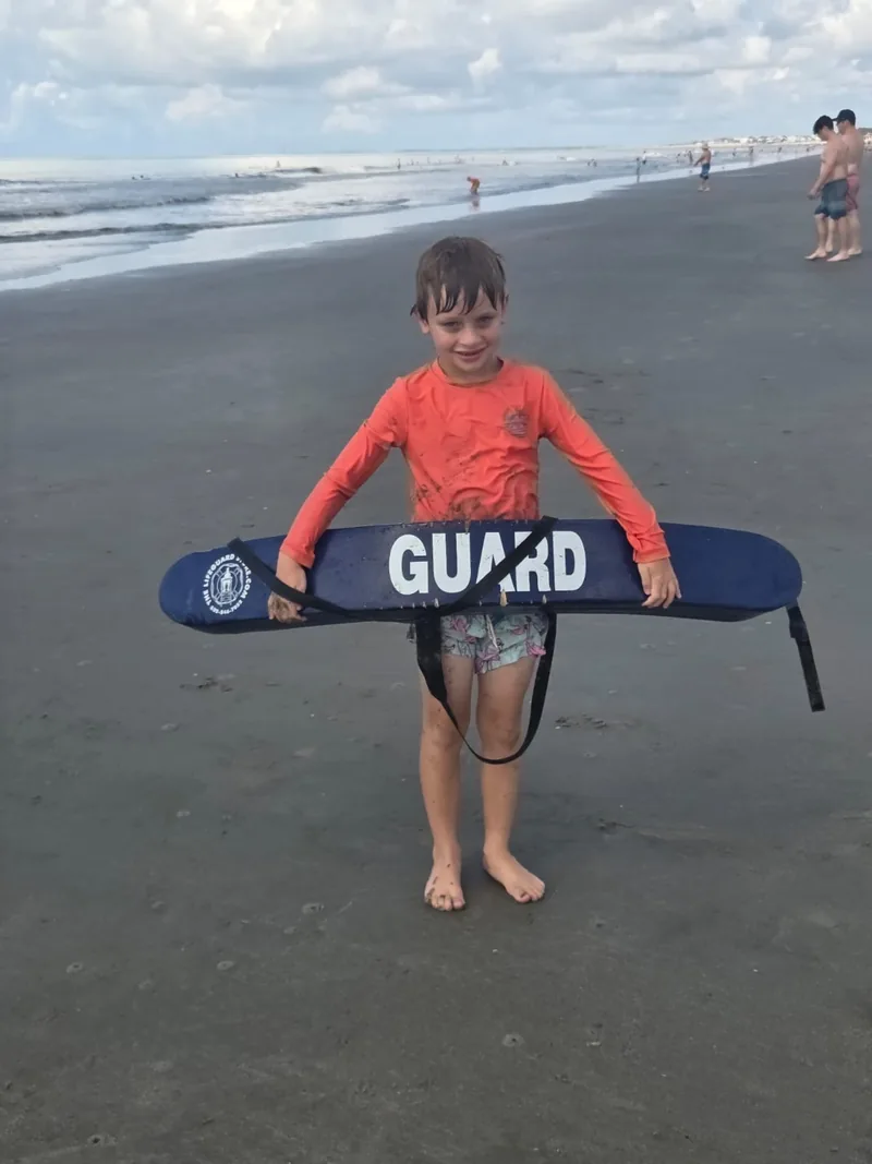 Young camper holding a lifeguard rescue tube on the beach