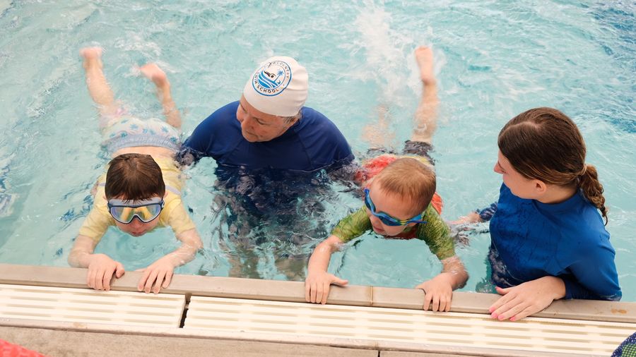 Young swimmers kicking at the pool wall with two instructors