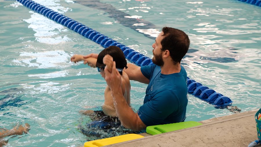 Instructor guiding a swimmer's arm stroke next to a lane line