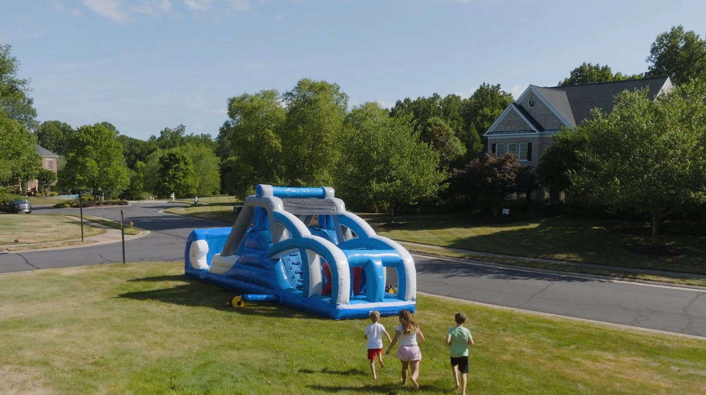 Three kids running toward a Cloud 9 obstacle course set up on a neighborhood lawn in Haymarket, Virginia