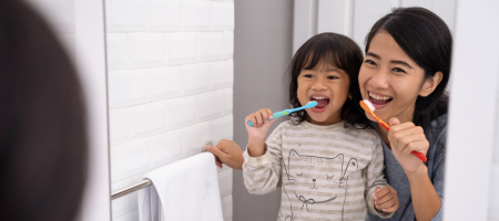 mom and daughter brushing teeth while looking in a mirror
