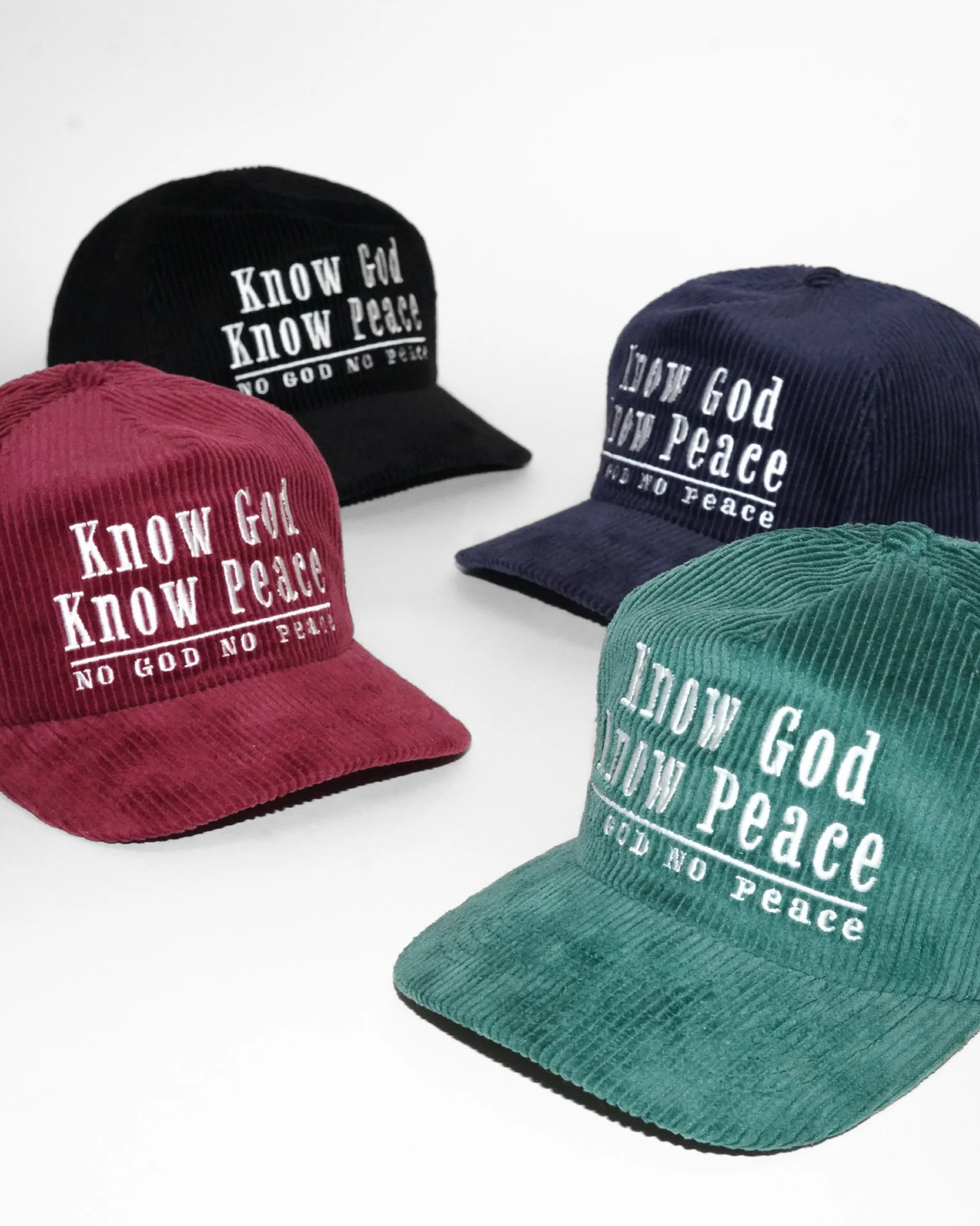 Four New Perspective corduroy hats in black, navy, burgundy and green, photographed against a white studio background.