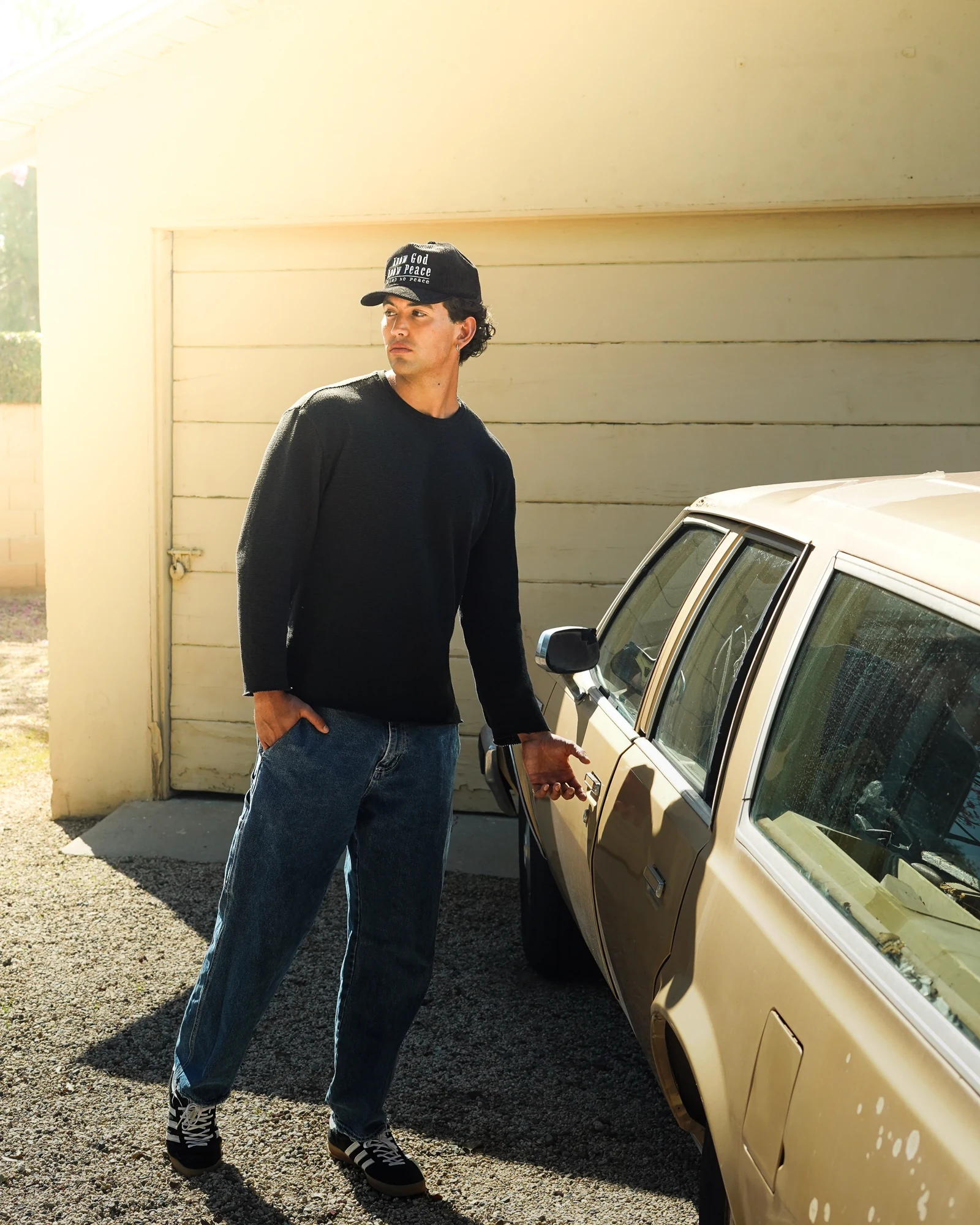 Model wearing a black New Perspective hat and dark top beside a vintage car in warm sunlight.