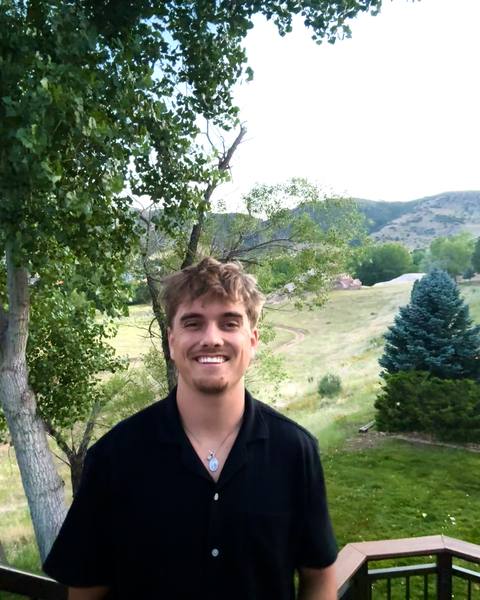 Rowdy Yates smiling outdoors, with trees and hills behind him.