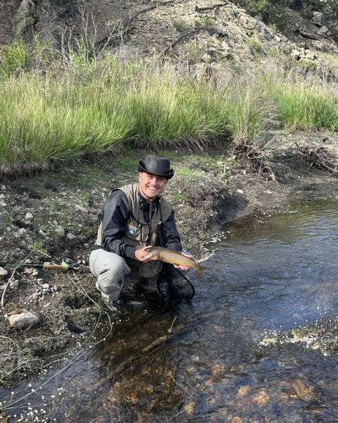 An angler kneeling in a stream and holding a fish.