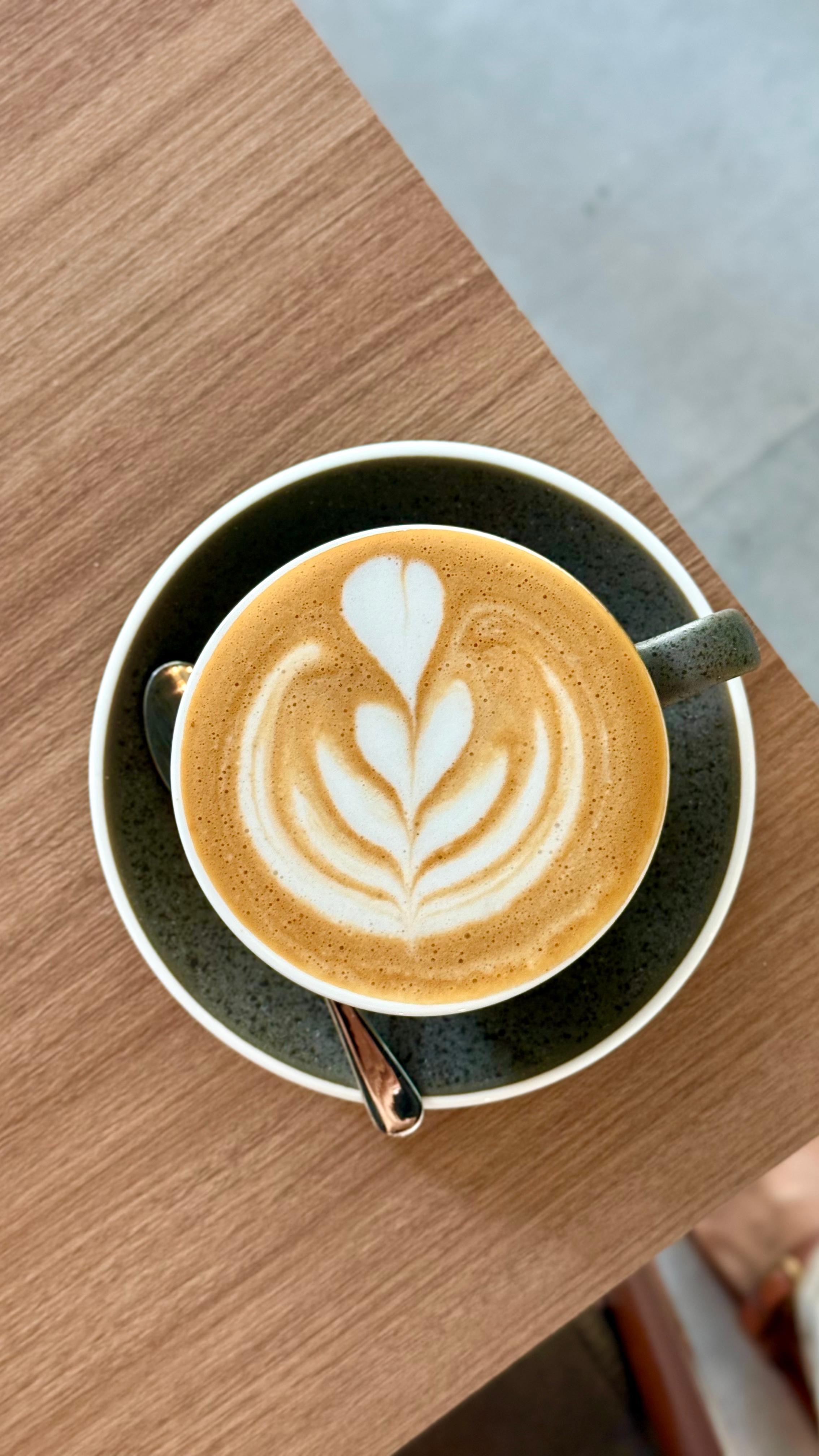 Latte art cappuccino served in a dark green cup on a wooden table at Adina’s Coffee Shop Dubai