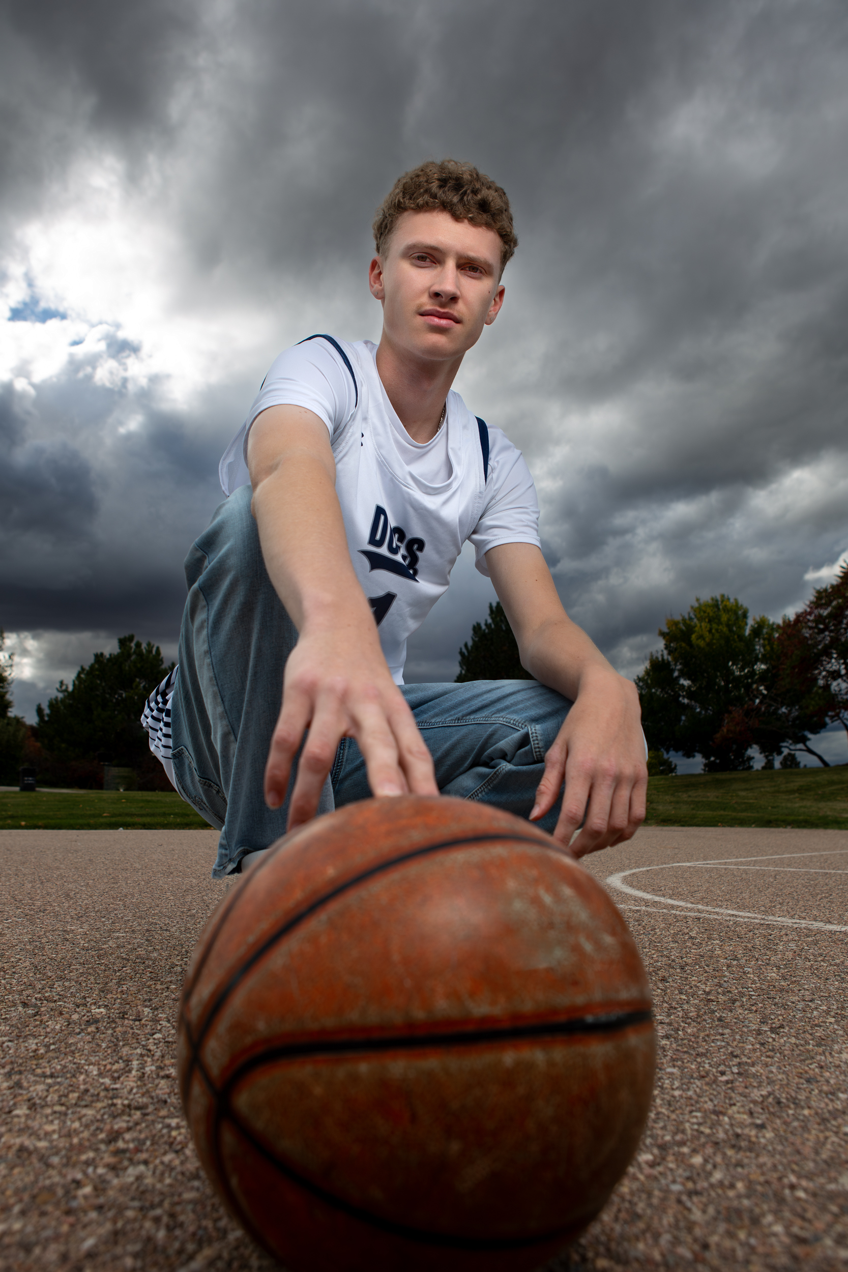 Senior boy leaning over a basketball with stormy sky Greeley Colorado senior portrait photographer