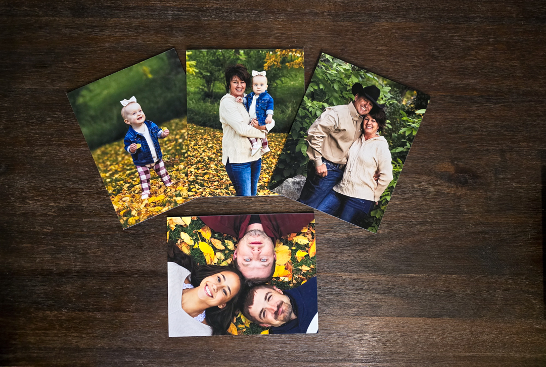 Four fine art portrait prints fanned out on a wood table showing family and couple photos Northern Colorado photographer