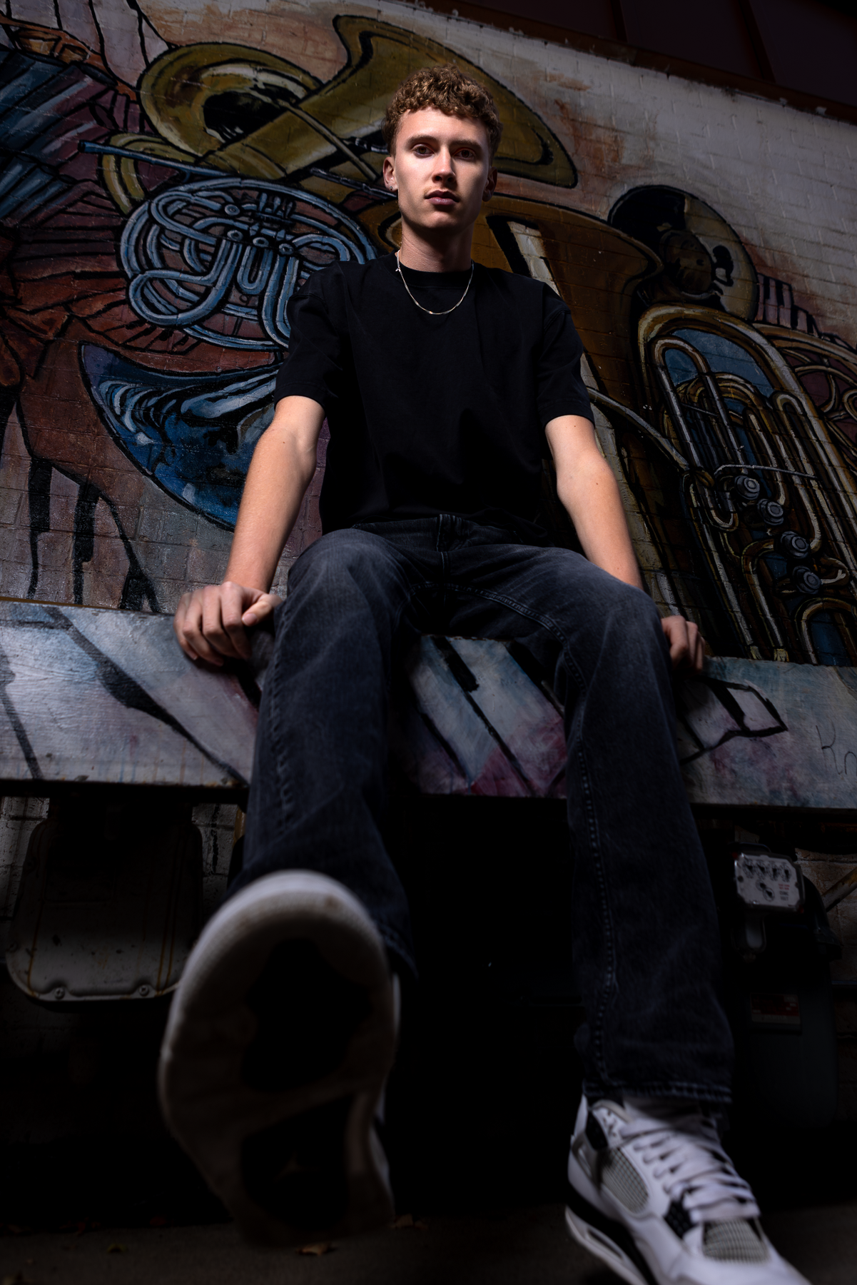 Senior boy in all black sitting in front of a colorful mural greeley colorado portrait photographer