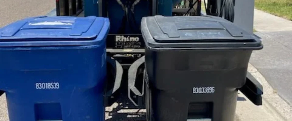 A bright blue Rhino trash can and a black one standing side-by-side on a sunny day. A bright blue Rhino trash can and a black one standing side-by-side on a sunny day.