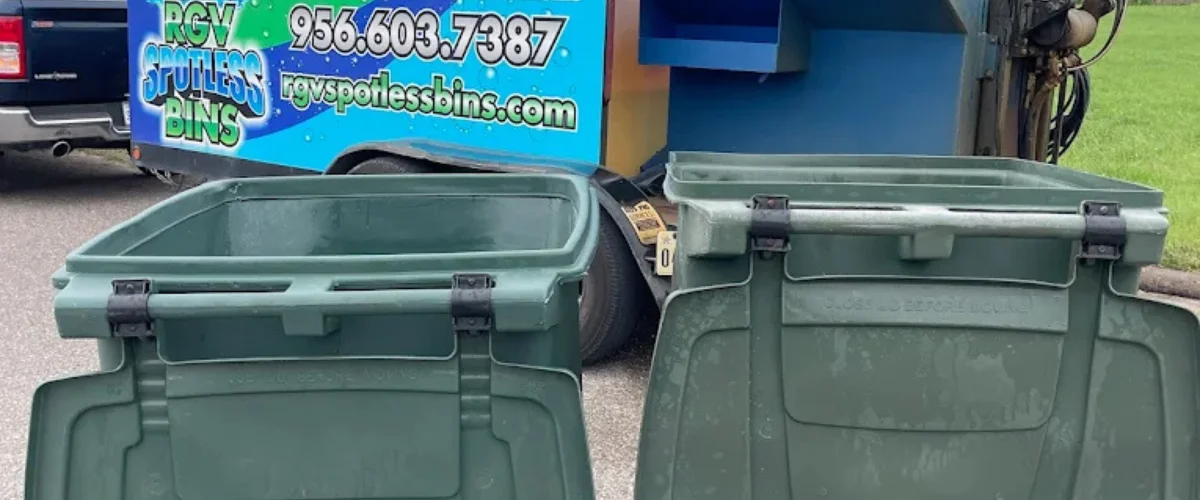 Two open, empty, dark green trash bins with black hinges, positioned next to a blue RGV Spotless Bins trailer.