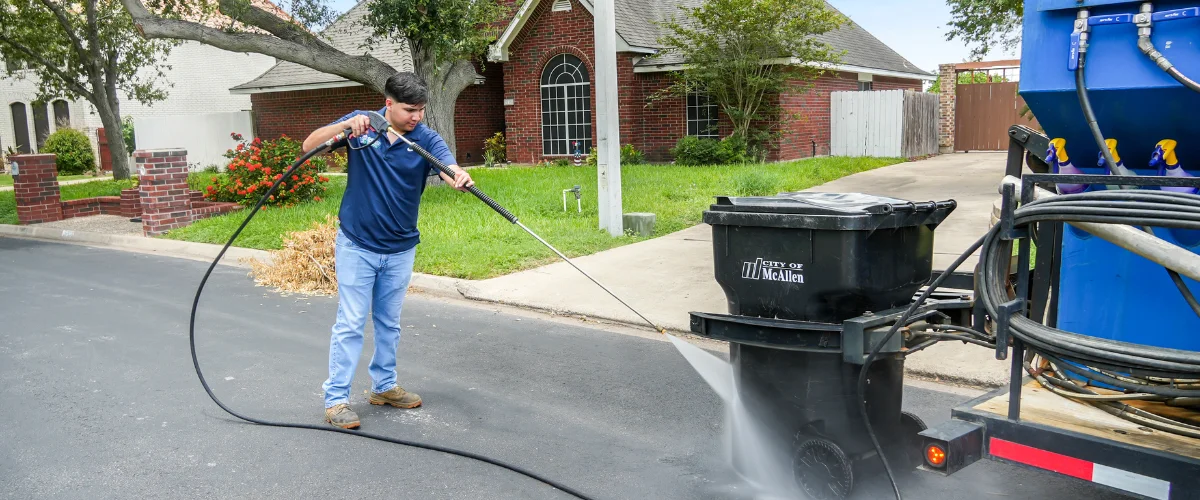 A man in blue jeans and a polo shirt power washing a black City of McAllen trash can on the street. A man in blue jeans and a polo shirt power washing a black City of McAllen trash can on the street.