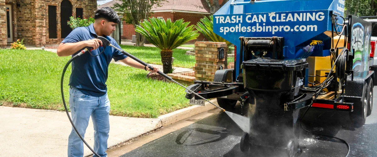 A black trailer with the "Spotless Bin Pro" logo and blue cleaning equipment parked on a residential street. A black trailer with the "Spotless Bin Pro" logo and blue cleaning equipment parked on a residential street.
