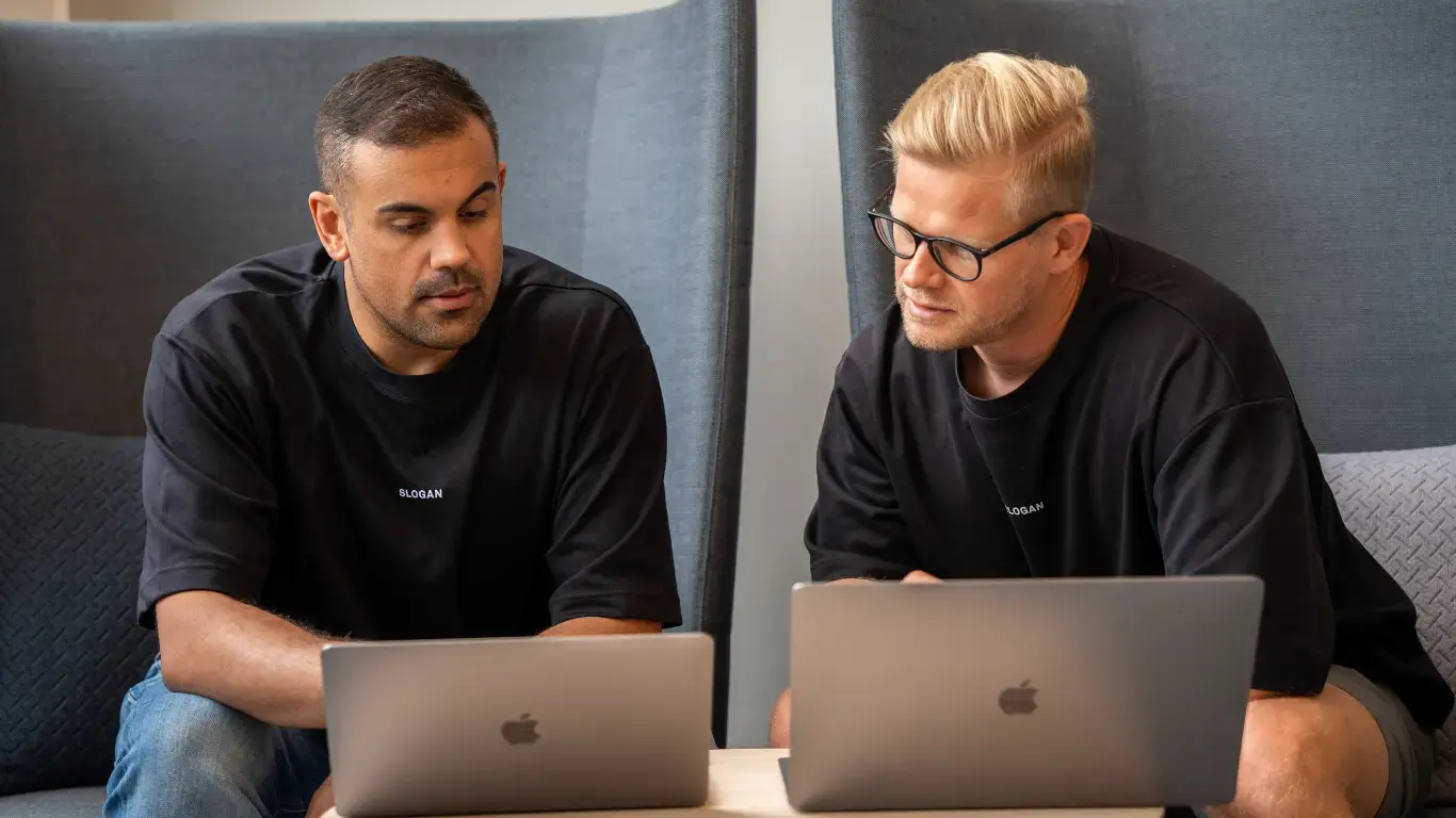 Sloganin perustajat Emir Rebiai ja Olli Ropponen työskentelemässä Apple MacBook -kannettavilla tietokoneilla modernissa toimistossa.