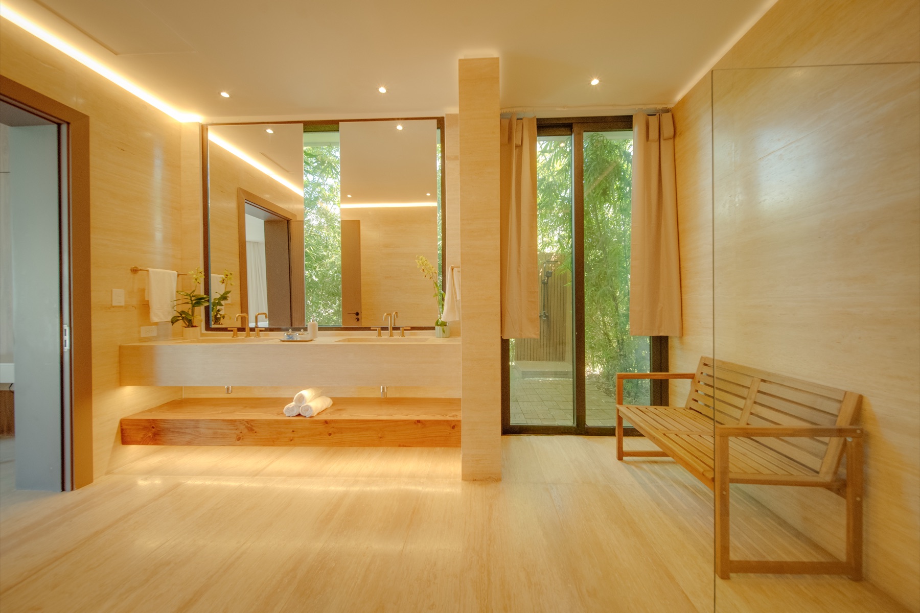 Primary bath in travertine with floating vanity and teak bench