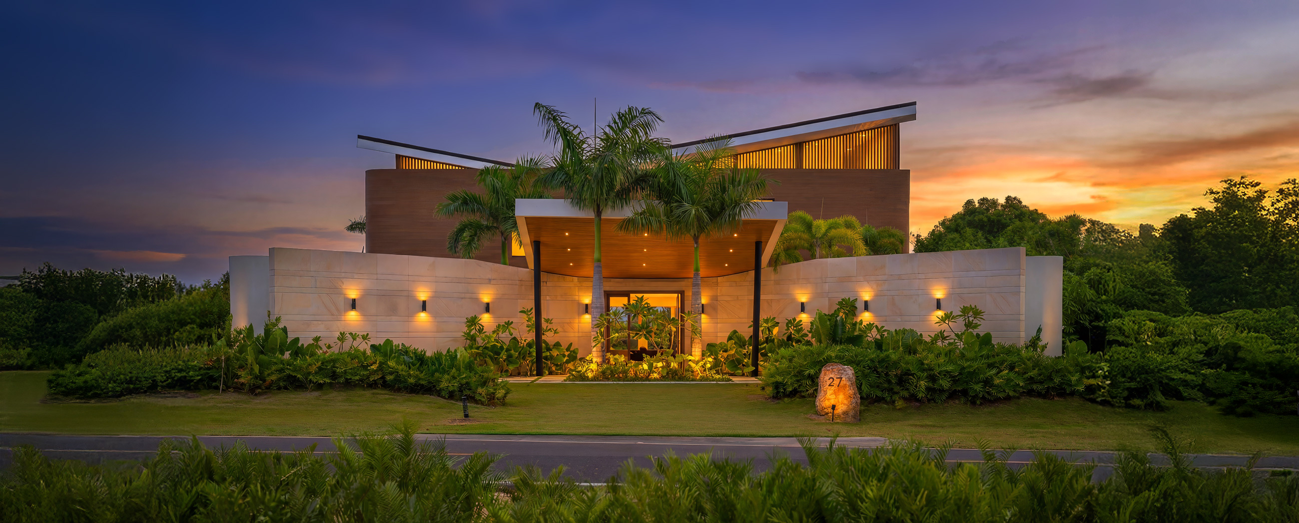 Villa Veintisiete at twilight, Casa de Campo: lit stone wall, palms, and butterfly roof against the sunset