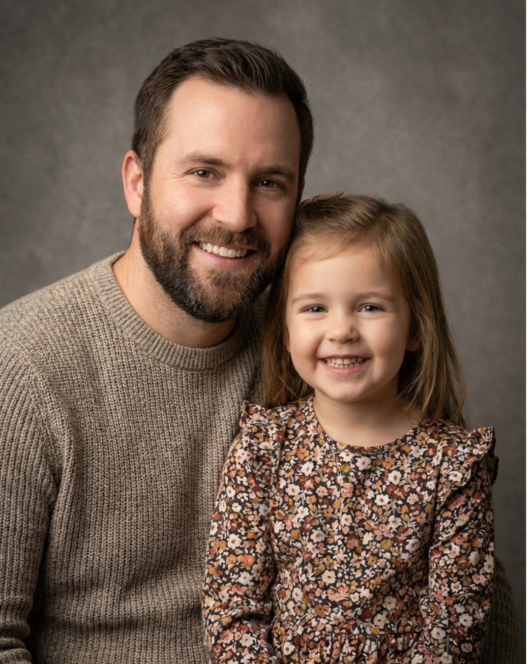 A professional studio portrait of a smiling father and his young daughter posing together against a neutral background.
