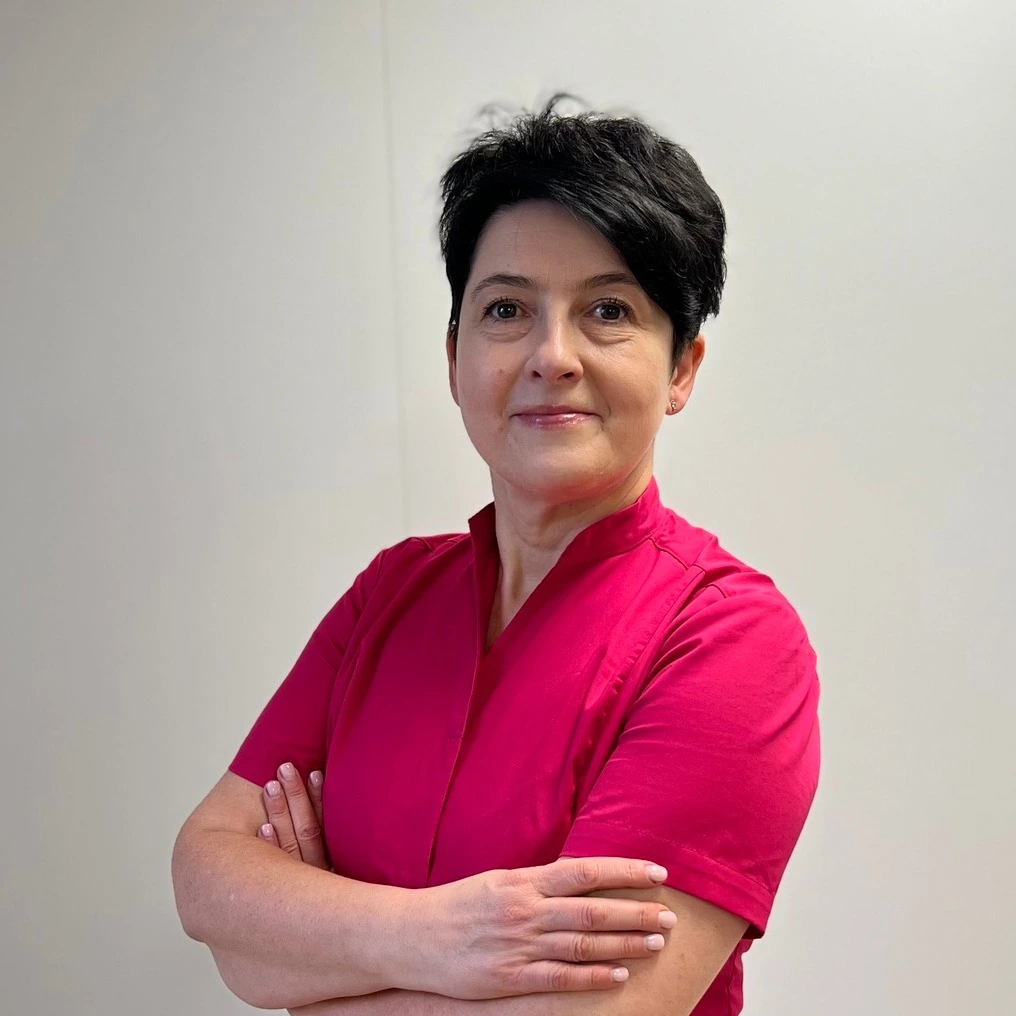 Aesthetic clinic owner smiling warmly inside her treatment room, wearing a professional uniform
