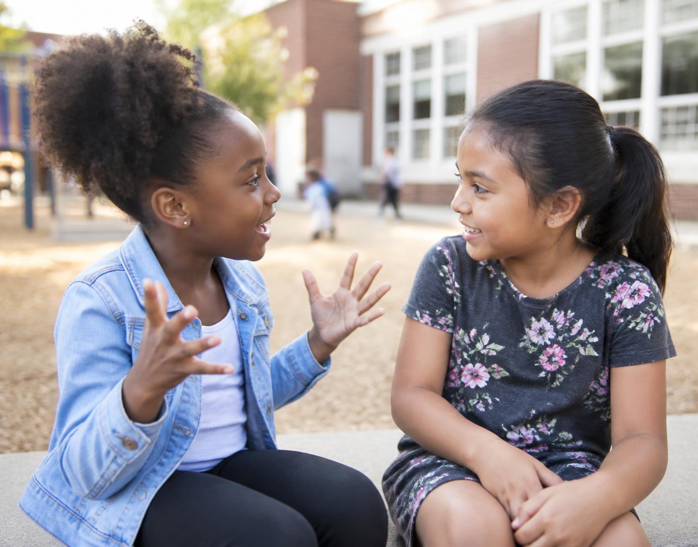 Two school aged children talking together outside their school.