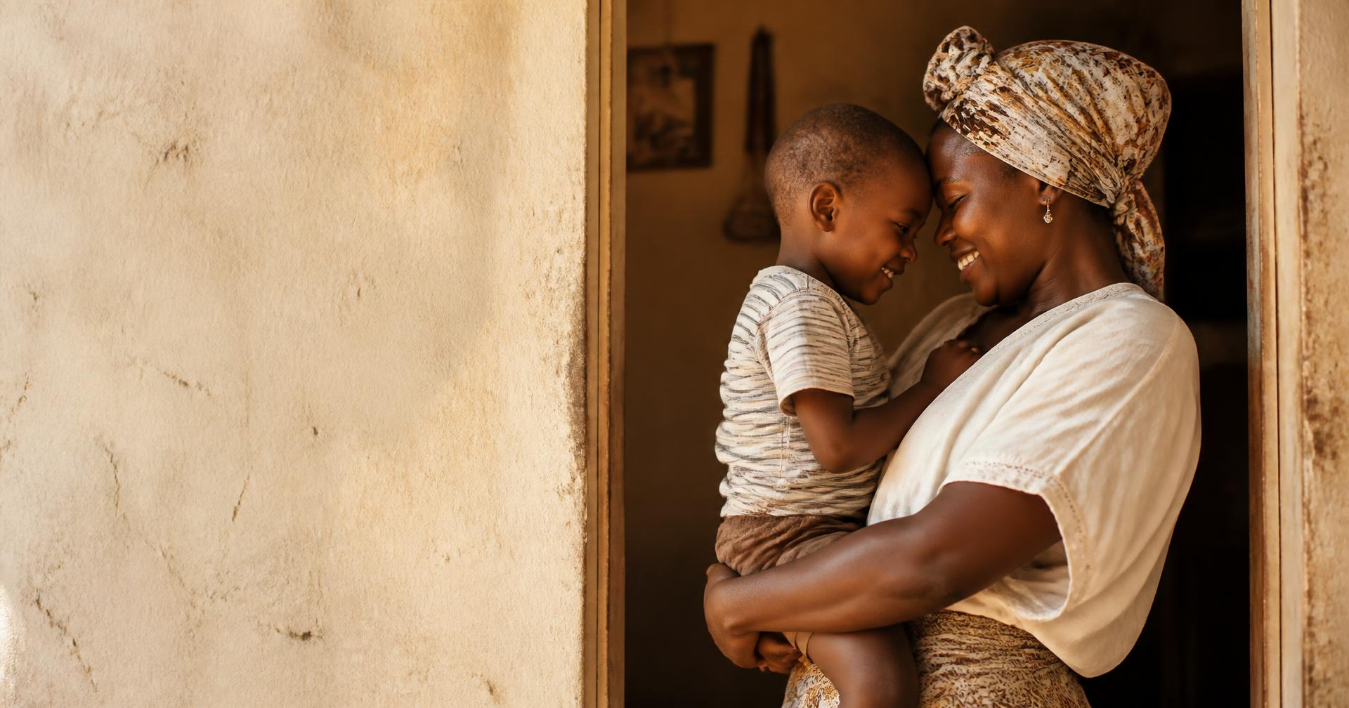 A mother holding her young son close in a sunlit doorway.