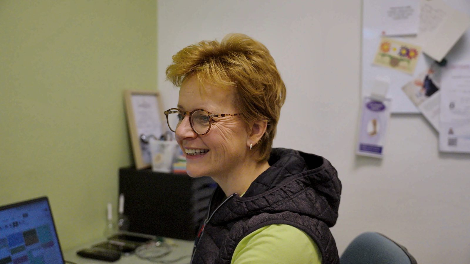 Sandra lacht aan haar bureau in de praktijk