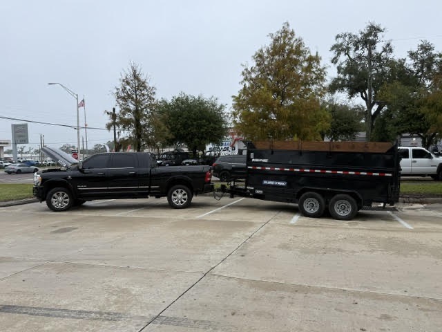Black pickup truck towing a dumpster trailer in a parking lot for hauling and dumpster rental services.