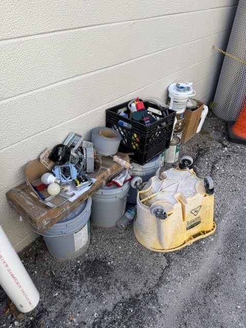 Construction debris, buckets, tools, and cleanup materials staged beside a commercial building during a property cleanup project.