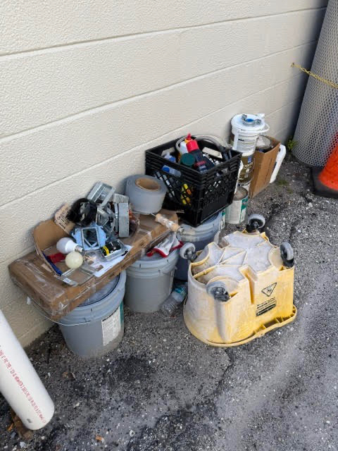 Construction debris, buckets, tools, and cleanup materials staged beside a commercial building during a property cleanup project.