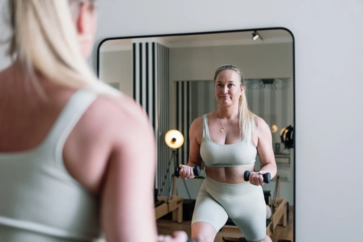A woman training with dumbbells, seen in the studio mirror