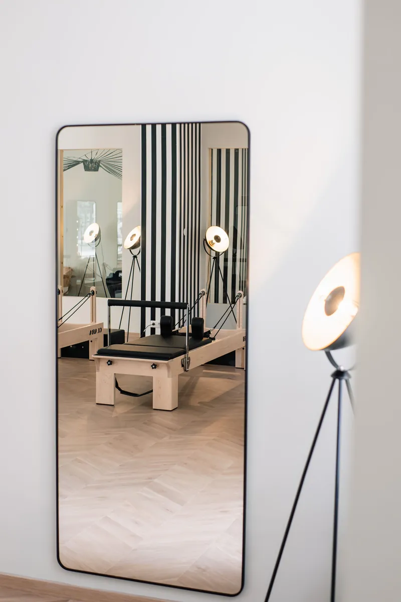 A Reformer reflected in a tall mirror next to a vintage spotlight lamp in the studio