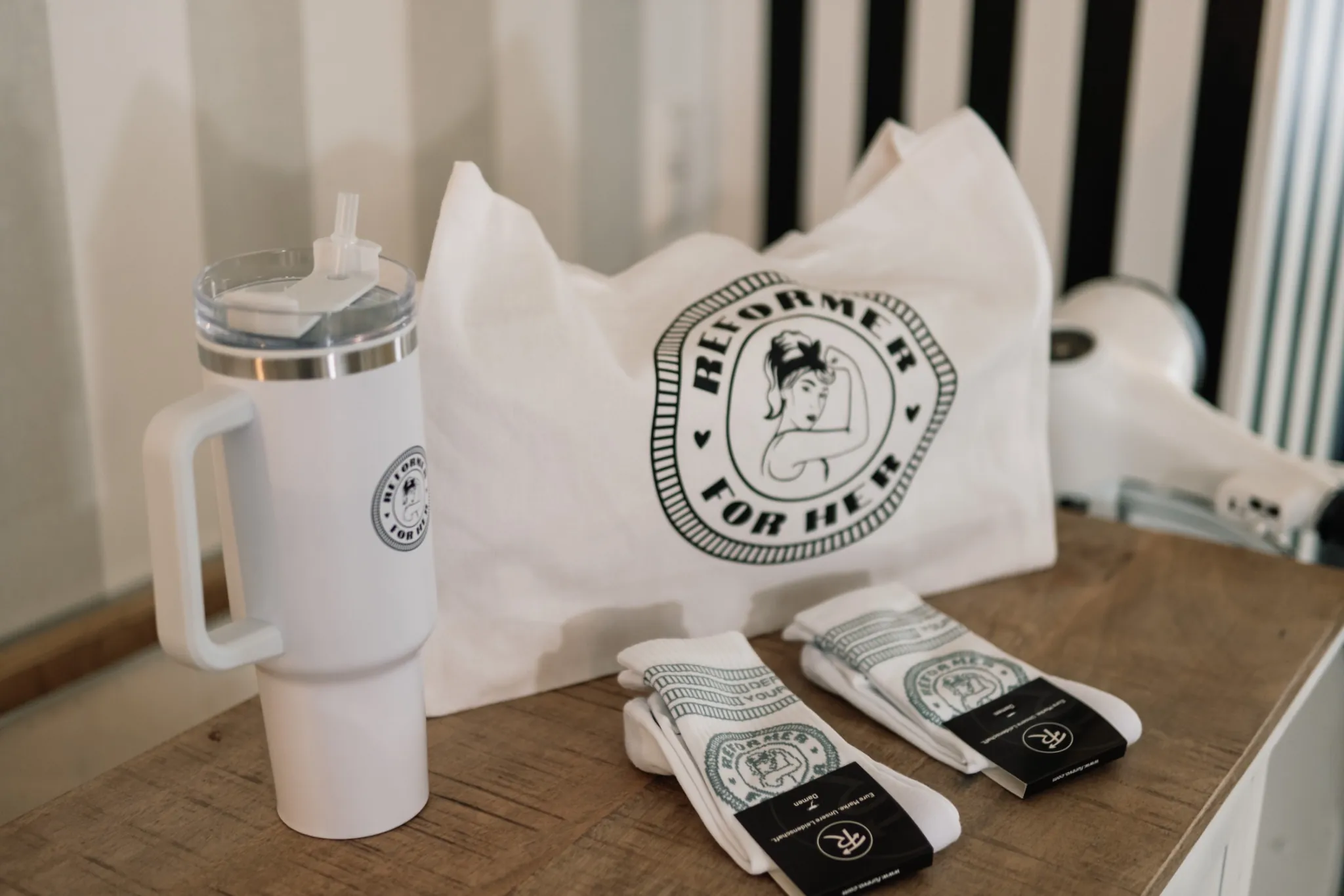 Reformer For Her tote bag, tumbler and grip socks on a wooden shelf