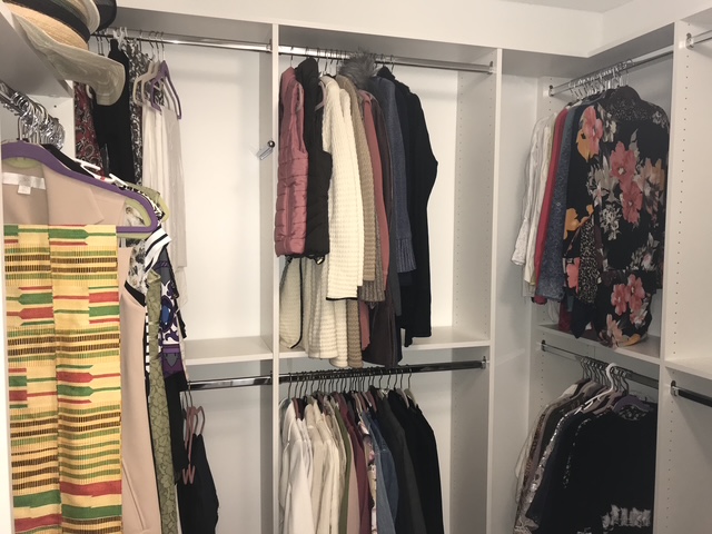 An organized walk-in closet with clothing arranged on tidy shelves and rails