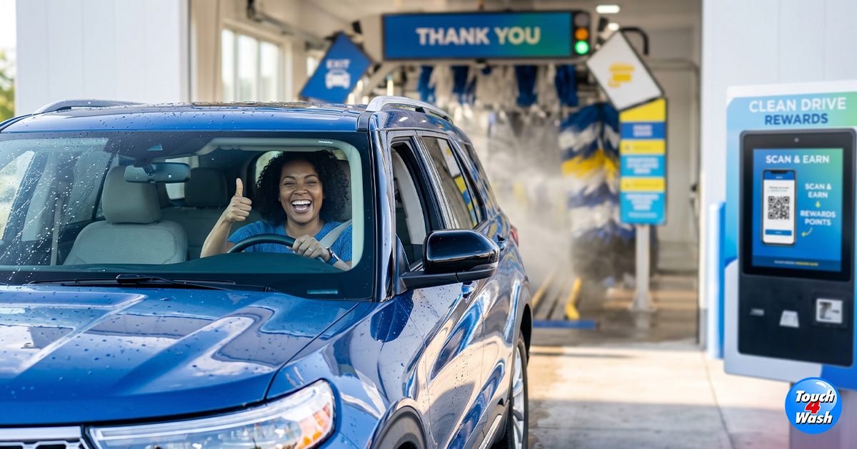 Happy customer giving thumbs up while driving blue SUV through automated car wash, featuring digital rewards kiosk and clean car loyalty program signage. Happy customer giving thumbs up while driving blue SUV through automated car wash, featuring digital rewards kiosk and clean car loyalty program signage.