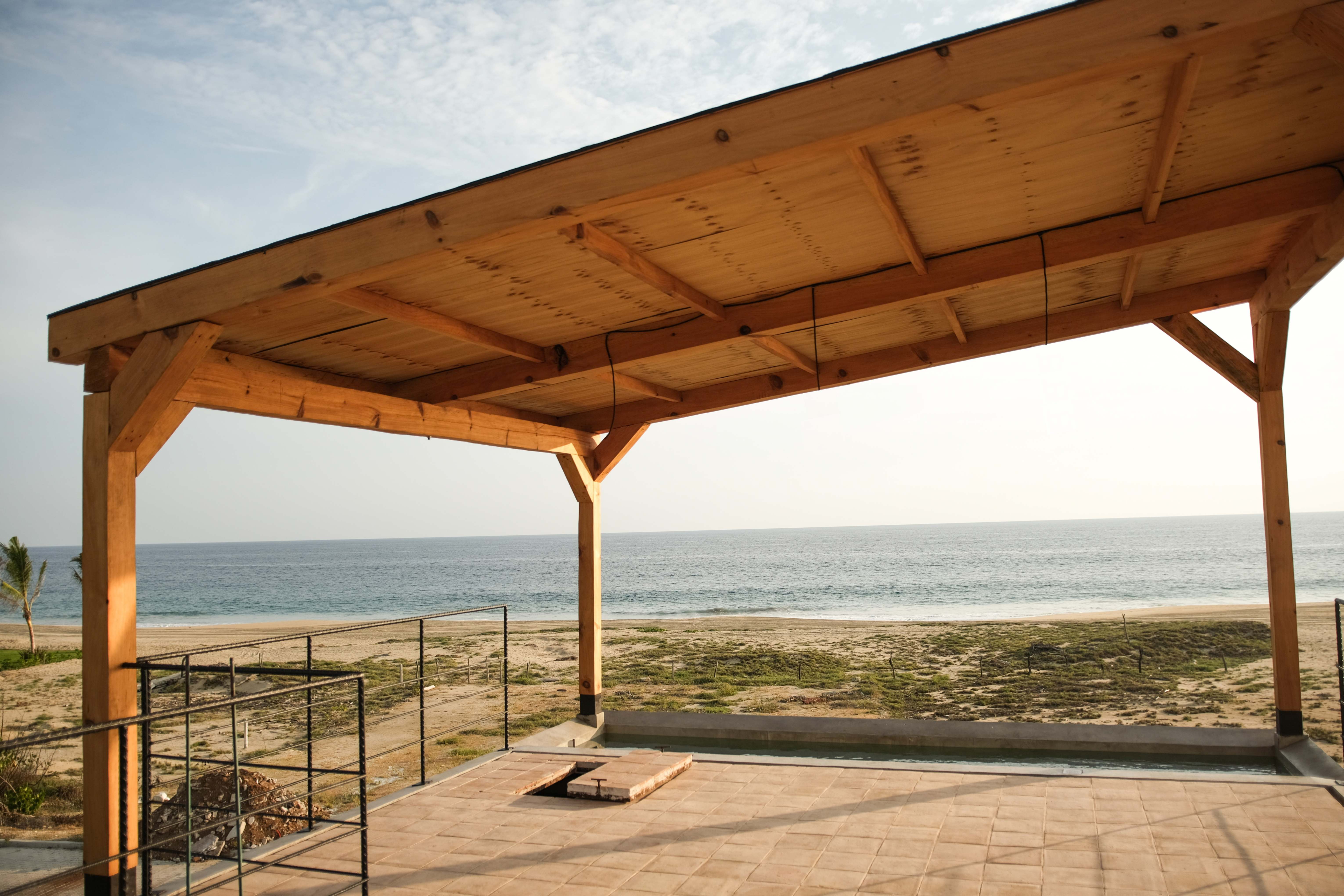 Wooden beam pavilion on a tiled terrace overlooking a sandy beach and ocean in Puerto Escondido, Oaxaca, Mexico.