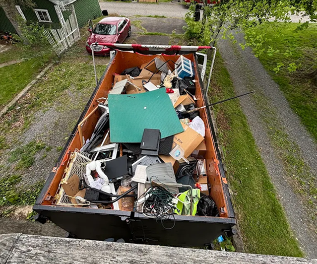 Overhead view of a full rental dumpster loaded with household junk, electronics, and furniture