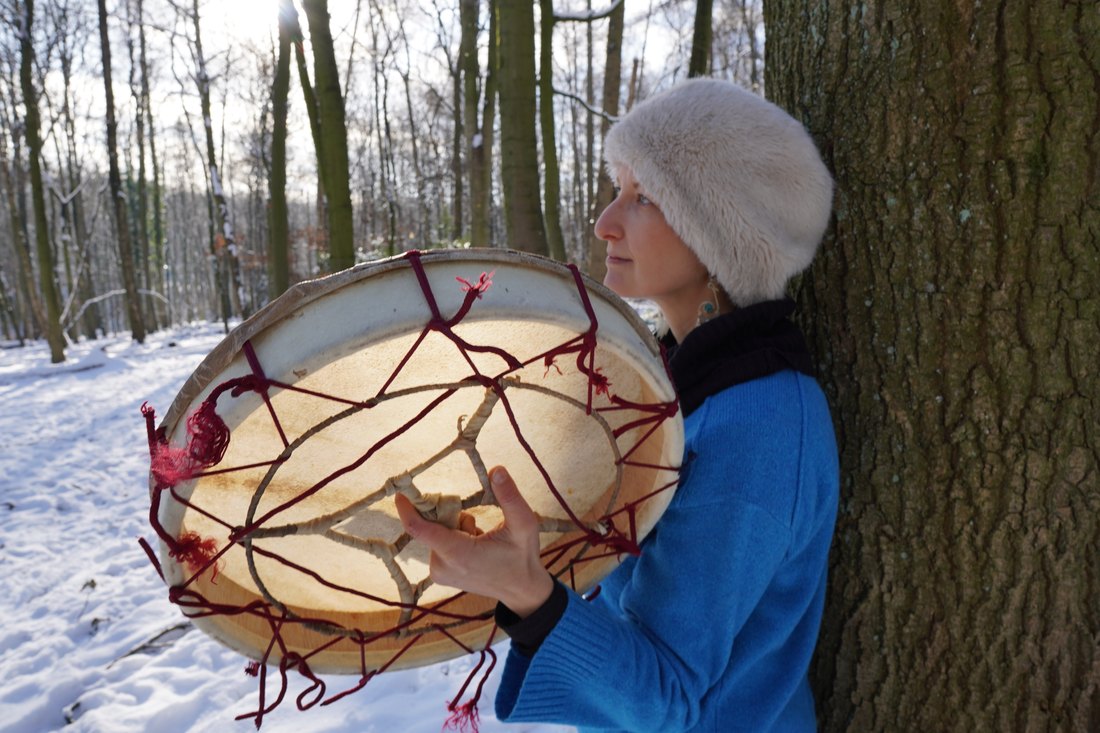 A frame drum held among snow-covered trees