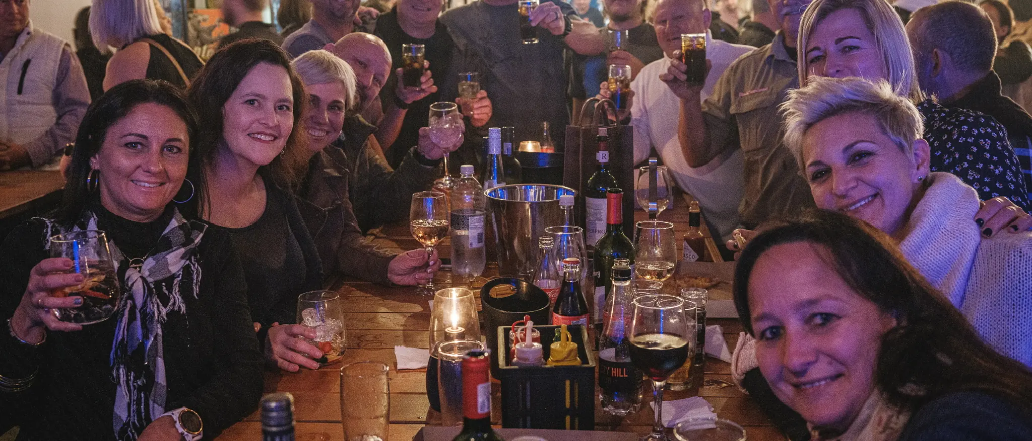 Long table of friends celebrating with drinks under festoon lights at Breezy's
