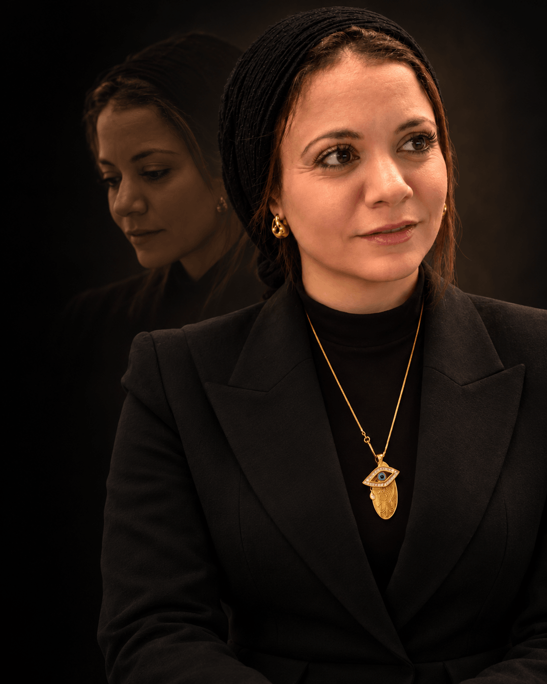 Dr. Sara Hegy in a black jacket and gold pendant looking into the distance, with a fainter image of her past self looking down behind her