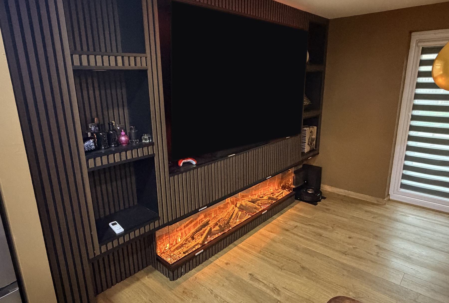 Dark slatted media wall with open shelving and a long electric fire