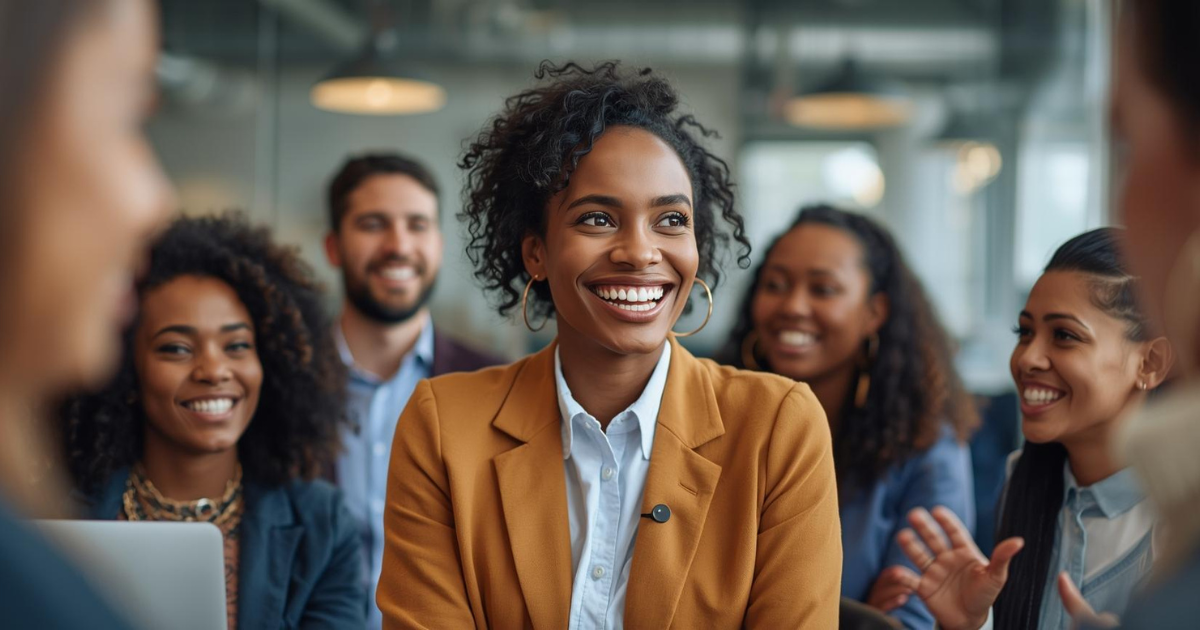 Smiling Black female leader sitting with a diverse group of coworkers in a modern, inclusive office setting