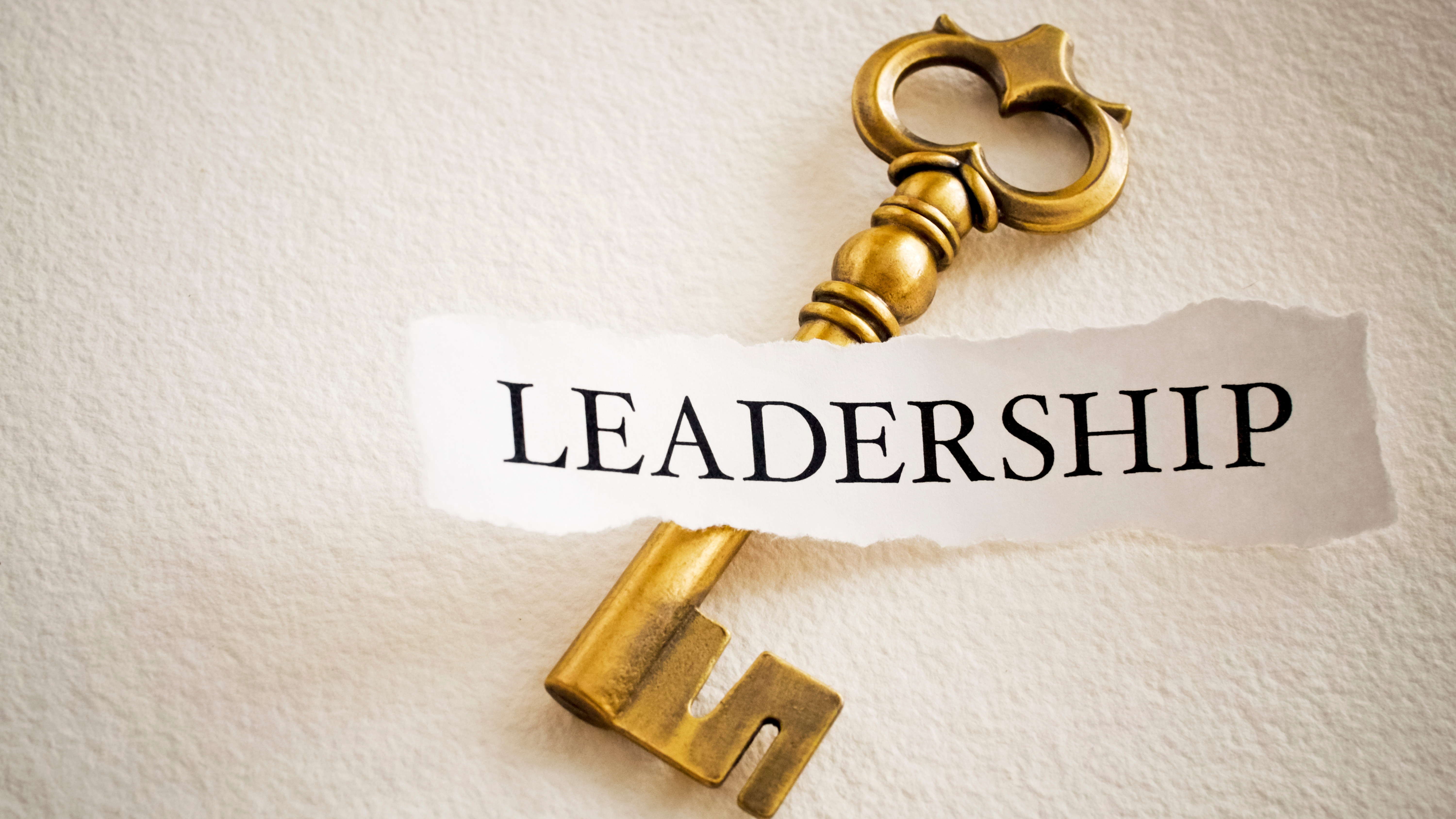 A brass key on a torn paper strip that reads Leadership