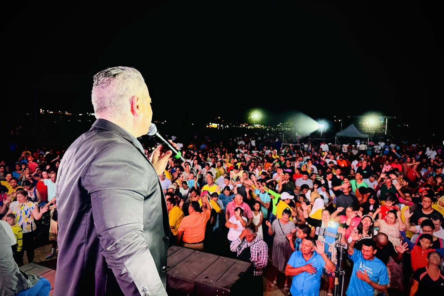 Speaking from a stage to a large outdoor crowd at night