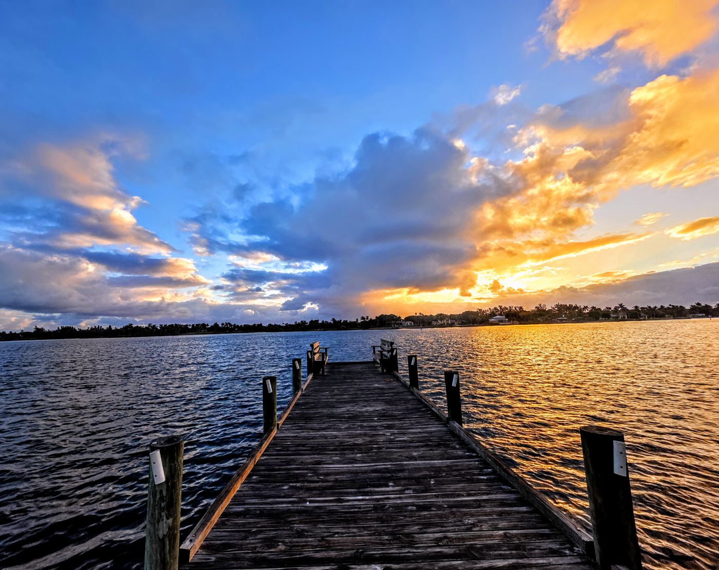 Weathered wooden dock leading into a river under a blue and gold sunrise sky