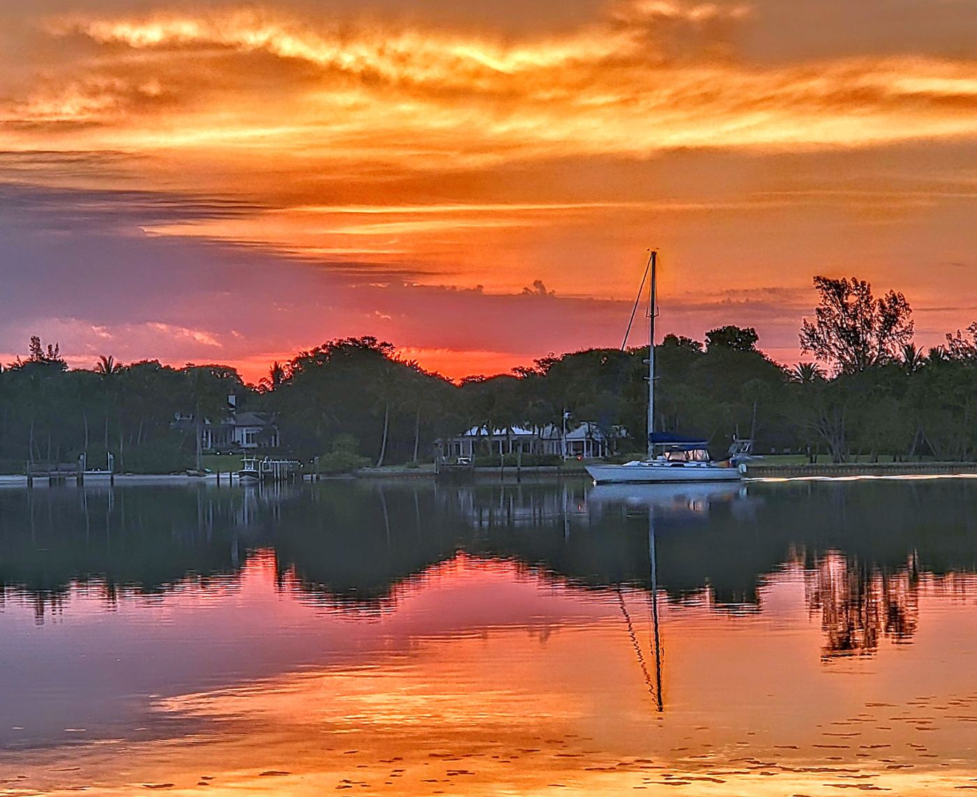 Sailboat anchored on glassy water reflecting an orange and pink Florida sunrise