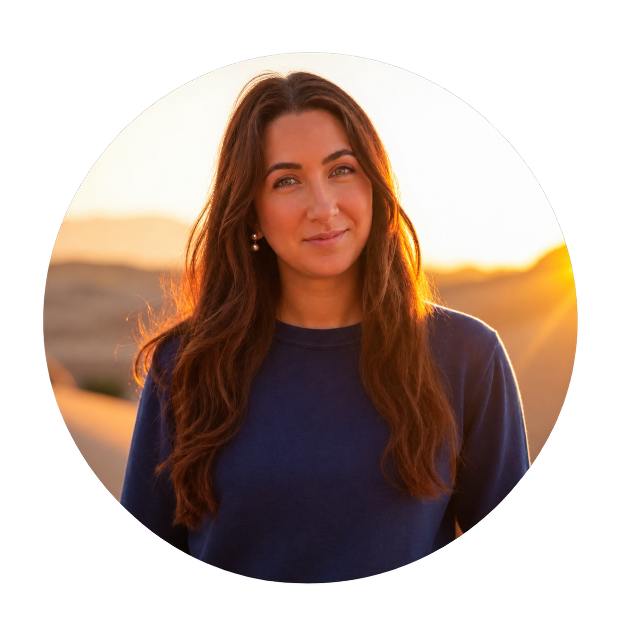 Esti, an auburn-haired woman in a navy sweatshirt and pearl earrings, standing in a desert canyon at golden hour