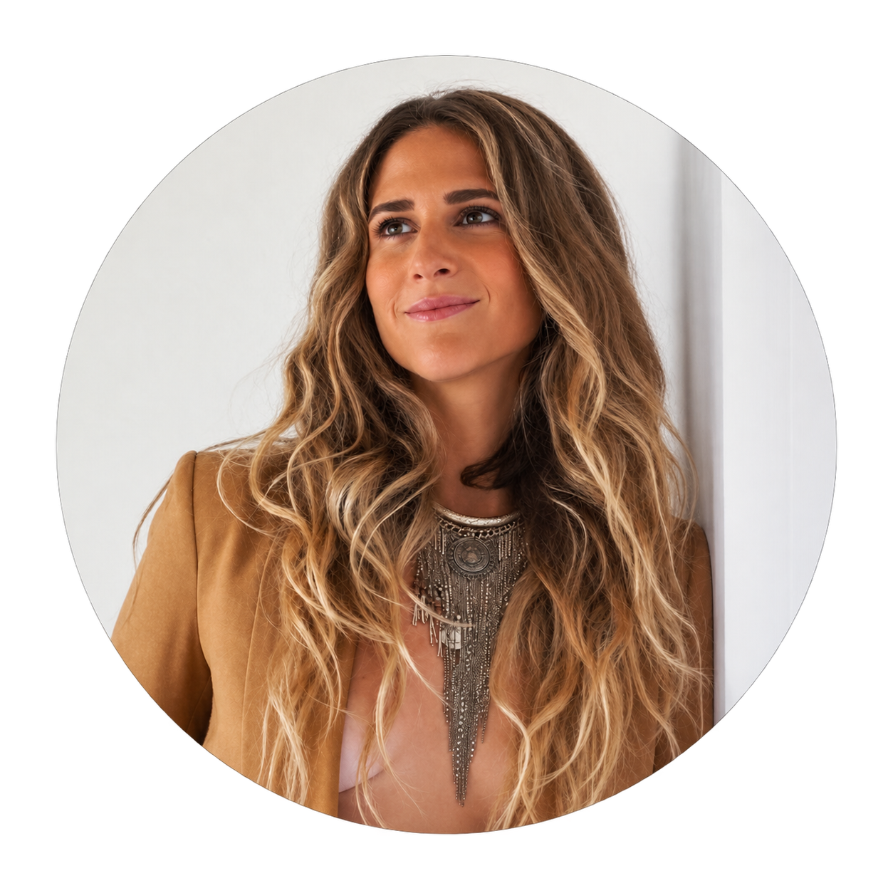 Jillian B, a woman with honey-blonde waves in a tan blazer and a large silver fringe necklace, looking up and away from the camera