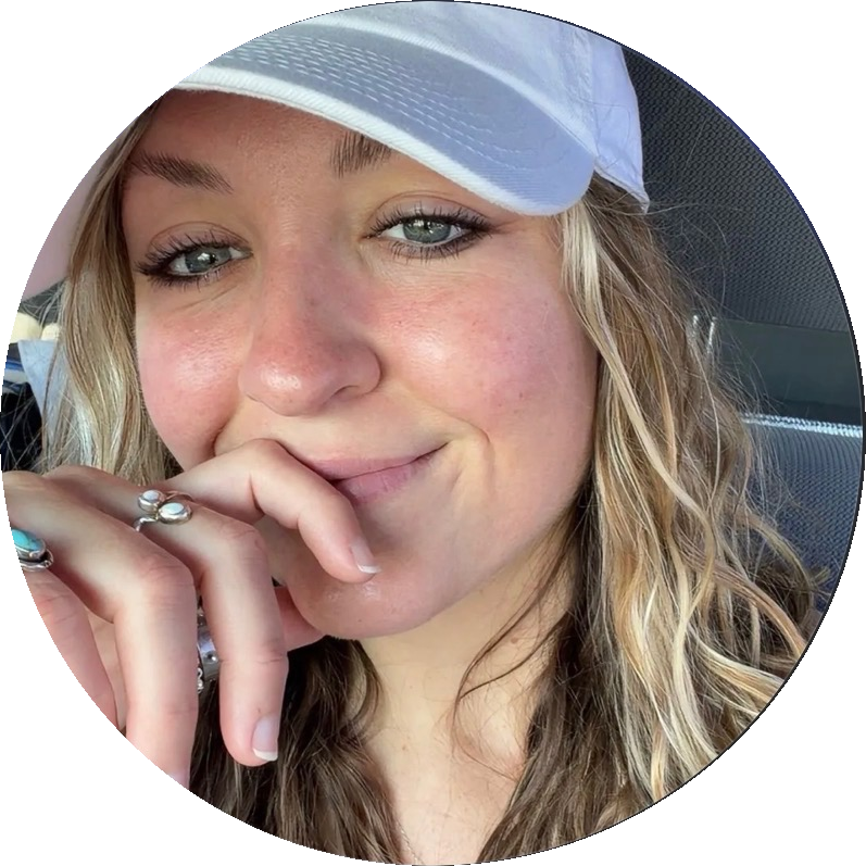 Sam Jo, a freckled blonde woman in a white cap seated in a car, her ringed hand resting near her chin
