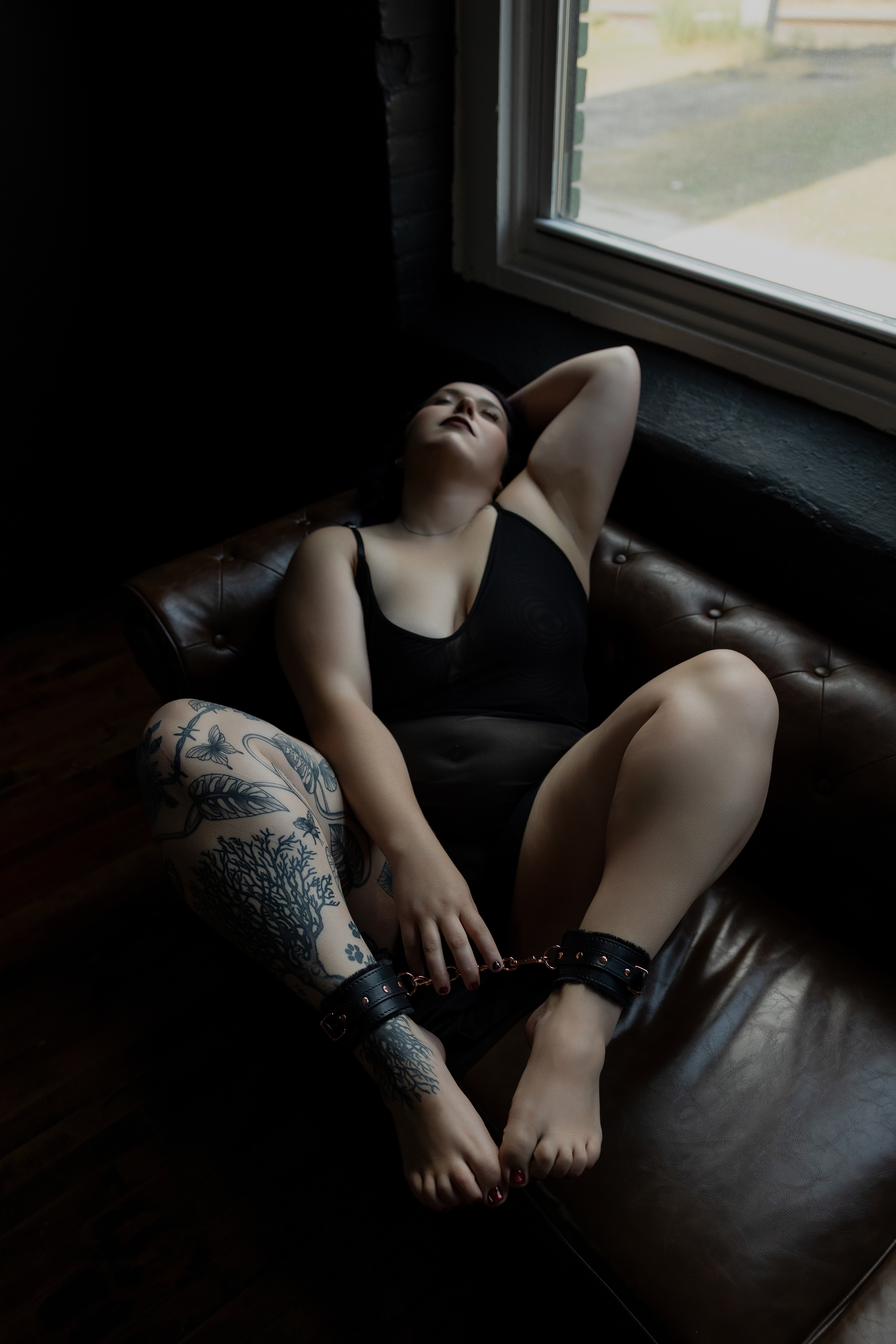Intimate boudoir portrait of a woman posed confidently on a leather sofa in a softly lit studio setting.