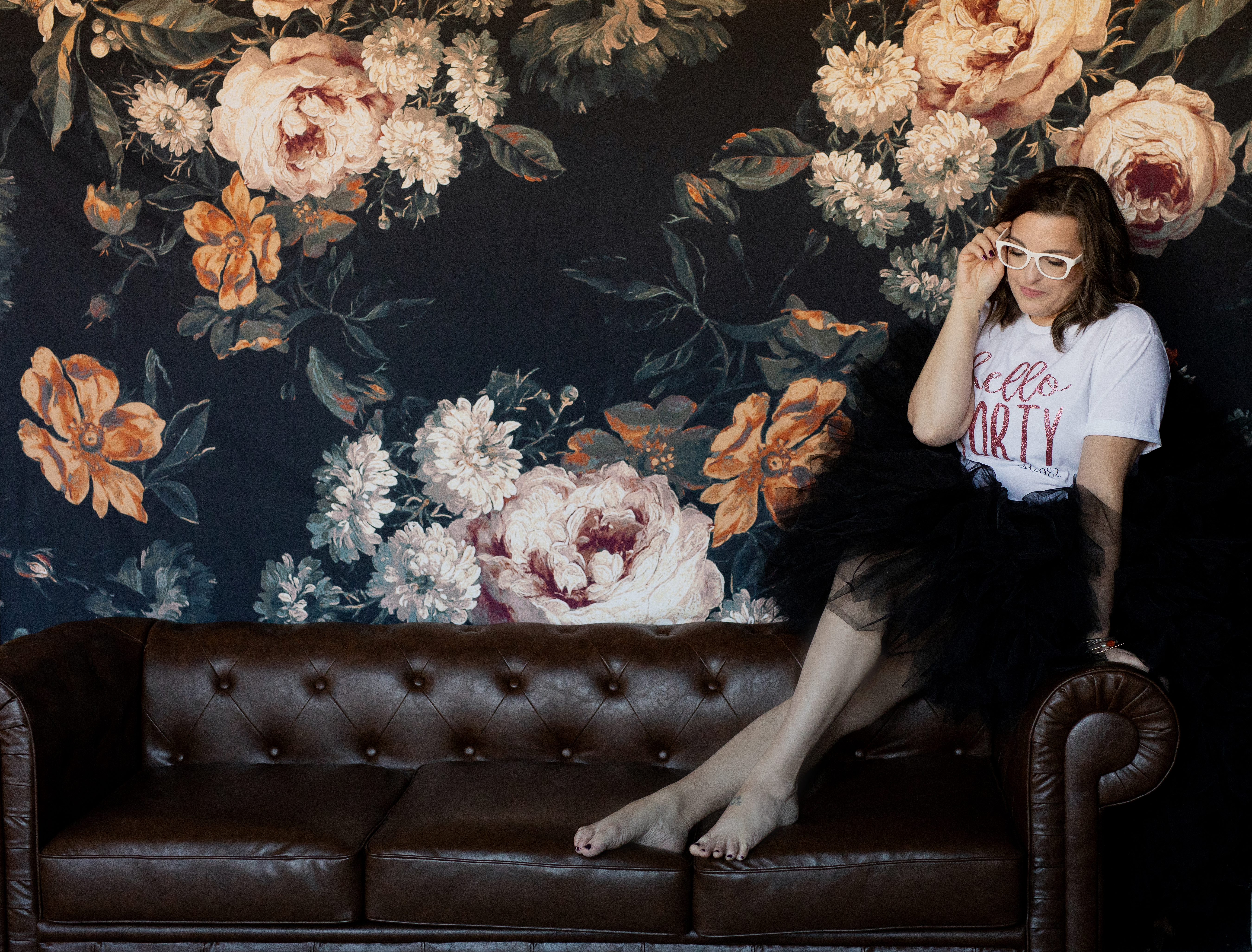 Elegant 40th birthday portrait featuring a woman in a “Hello Forty” shirt posed against a floral backdrop. Elegant 40th birthday portrait featuring a woman in a “Hello Forty” shirt posed against a floral backdrop.